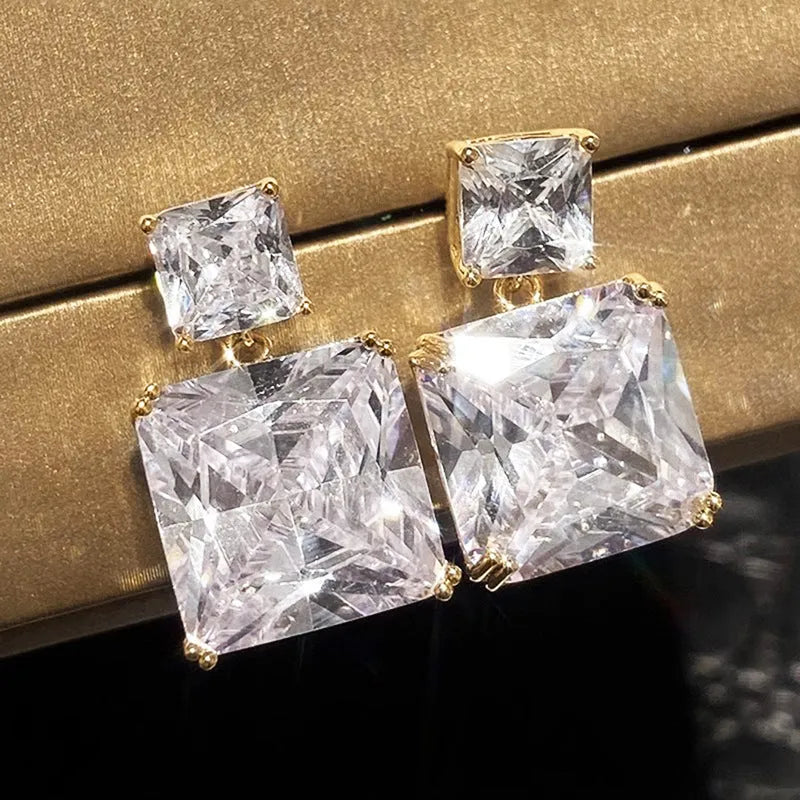 A pair of geometric square design earrings in a gold metallic finish on a white background.