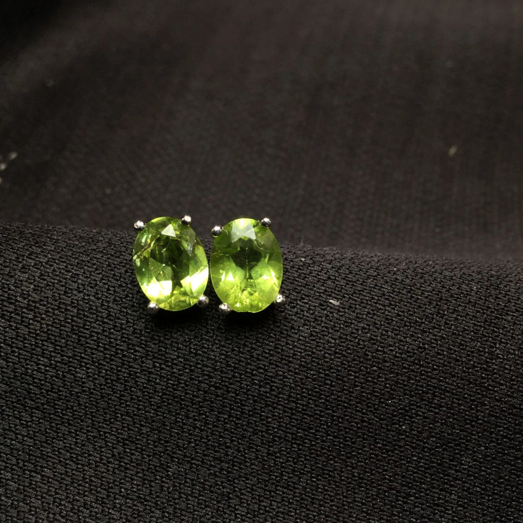 Close-up of grass green olivine stud earrings with elliptical 6x8mm stones in sterling silver setting.