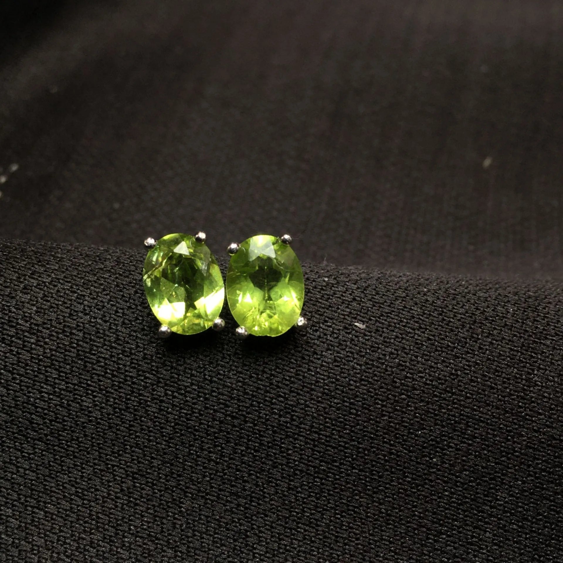 Close-up of grass green olivine stud earrings with elliptical 6x8mm stones in sterling silver setting.