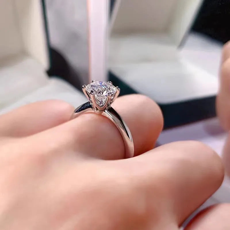 White gold plated six-claw zircon ring with a geometric design on a finger.