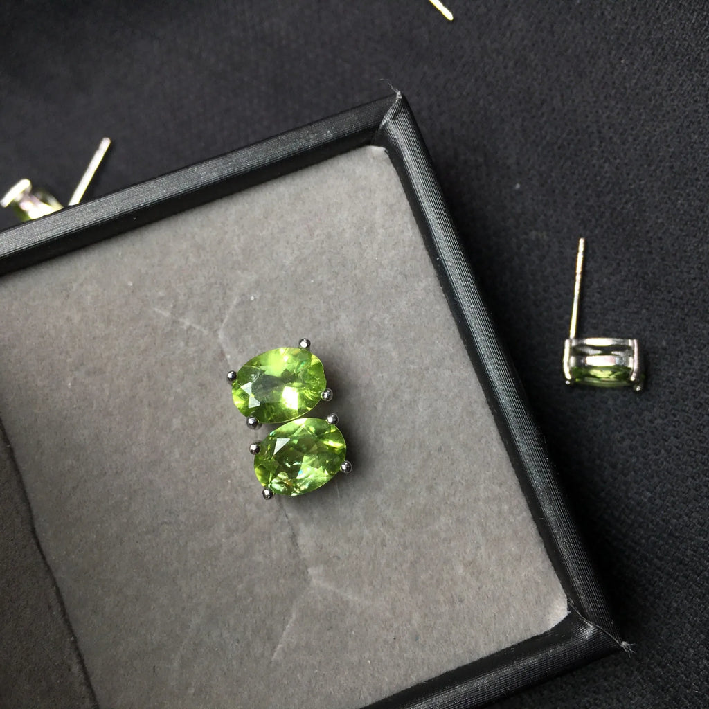Close-up of grass green olivine stud earrings with elliptical 6x8mm stones in sterling silver setting.