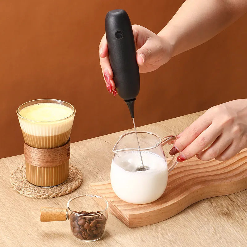 Hand-held milk frother with stainless steel whisk in modern black design creating microfoam in coffee cup
