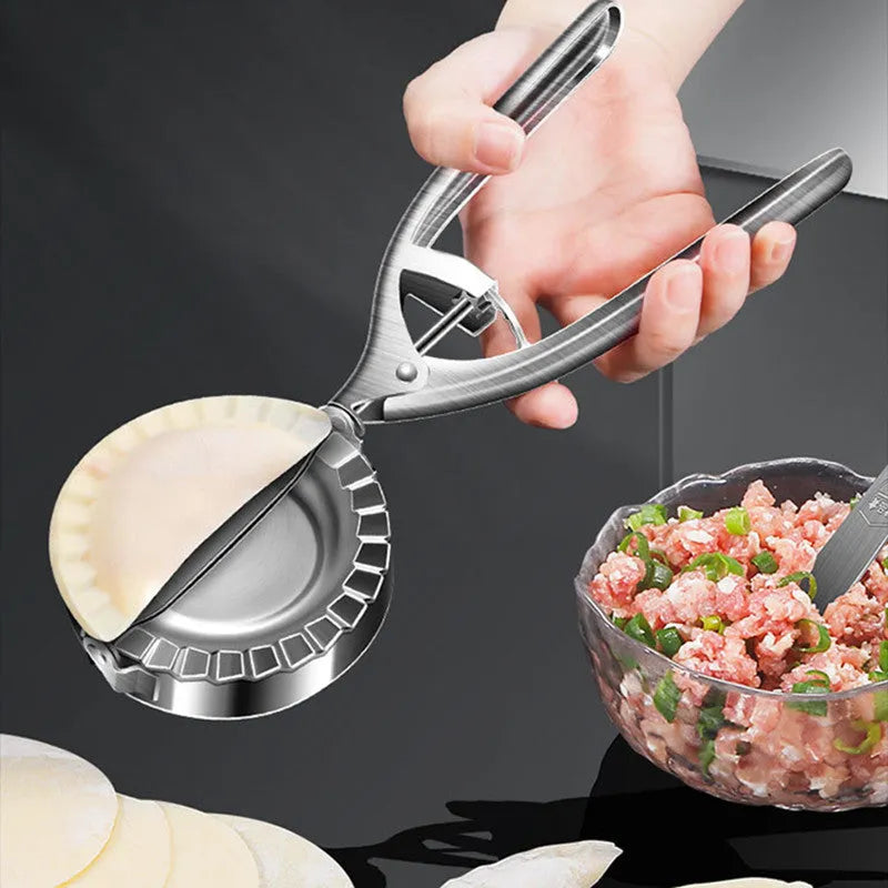 Silver stainless steel manual dumpling press mould with handle on a kitchen worktop.