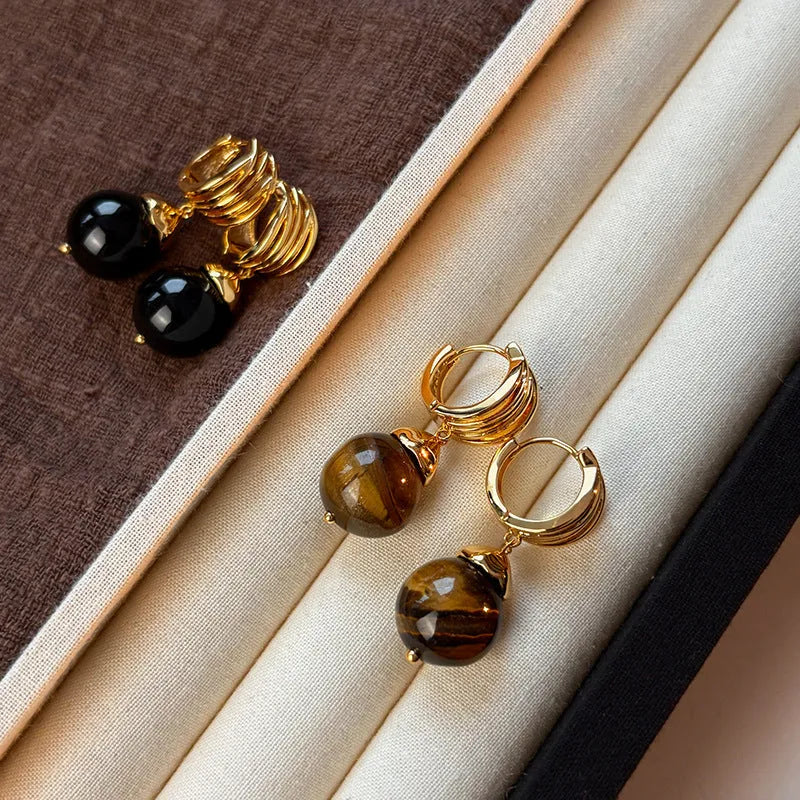 A pair of geometric tigereye stone earrings with 18K gold plating, showing natural brown bands, on a grey background.