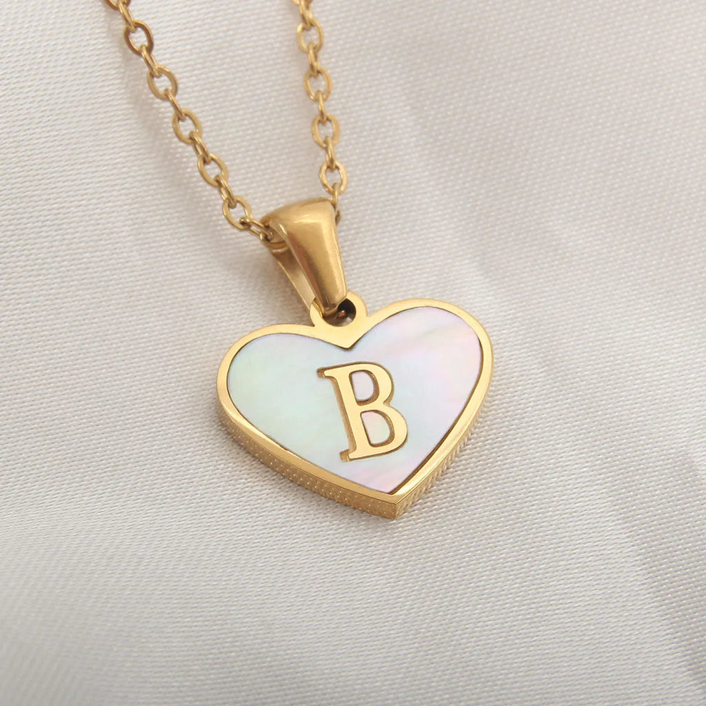 Gold-plated heart-shaped white shell initial necklace on a model, showing the adjustable clavicle chain.