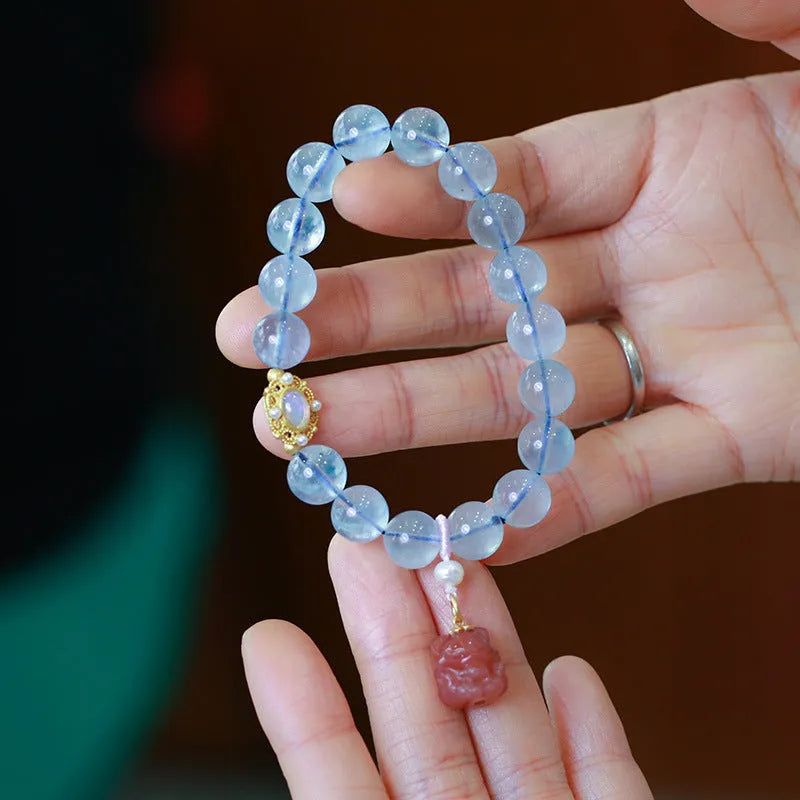 DIY aquamarine Fengjiu charm bracelet components laid out for assembly, showing pearls and pink crystals.
