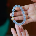 DIY aquamarine Fengjiu charm bracelet components laid out for assembly, showing pearls and pink crystals.