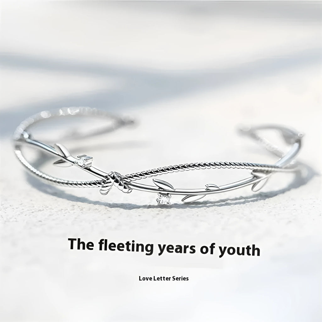 Close-up of an adjustable white gold coloured copper bracelet with a twisted branch and sprout design.