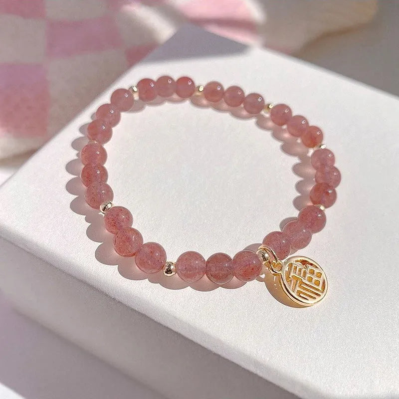Handmade strawberry quartz style glass bead bracelet with a blessing card charm on a wrist.