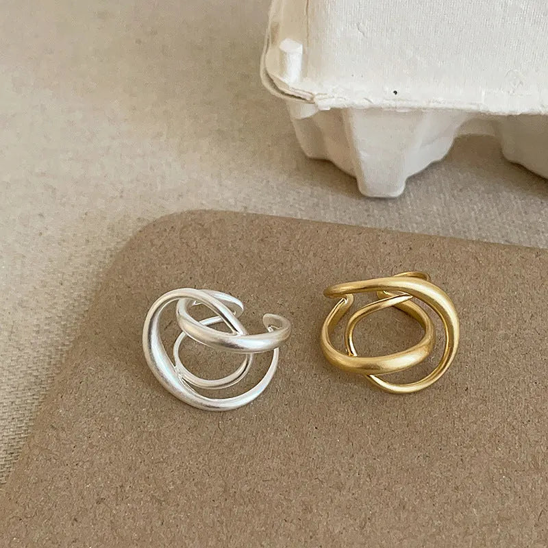 Adjustable geometric open ring with three-dimensional interlaced design and matte finish, shown in gold and silver colour options