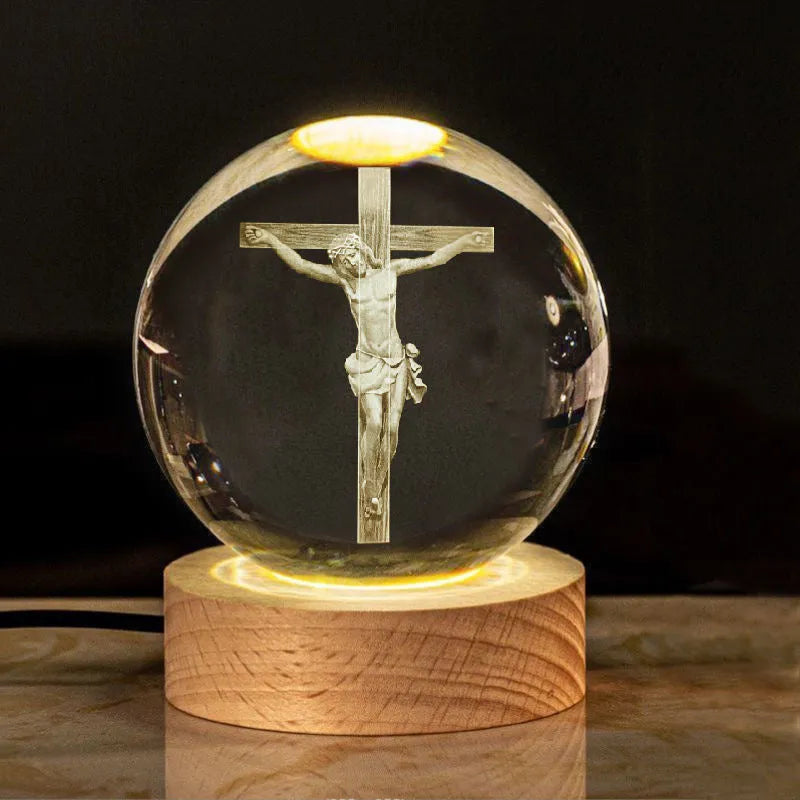 White crystal sphere on wooden base with warm glow, showing religious symbols including cross and prayer hands