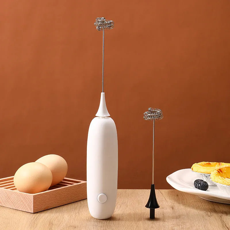 Hand-held milk frother with stainless steel whisk in modern black design creating microfoam in coffee cup