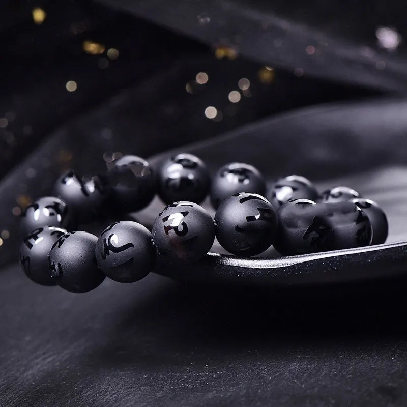 Natural frosted black agate bracelet with Sanskrit mantra and auspicious patterns, showing matte black stone glaze.