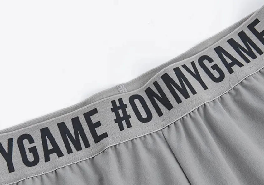 Loose fit grey sports cropped pants with a printed elastic waistband, shown on a model.