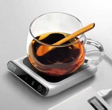 Black USB-powered cup warmer heating coaster with control buttons on a desk next to a coffee mug.