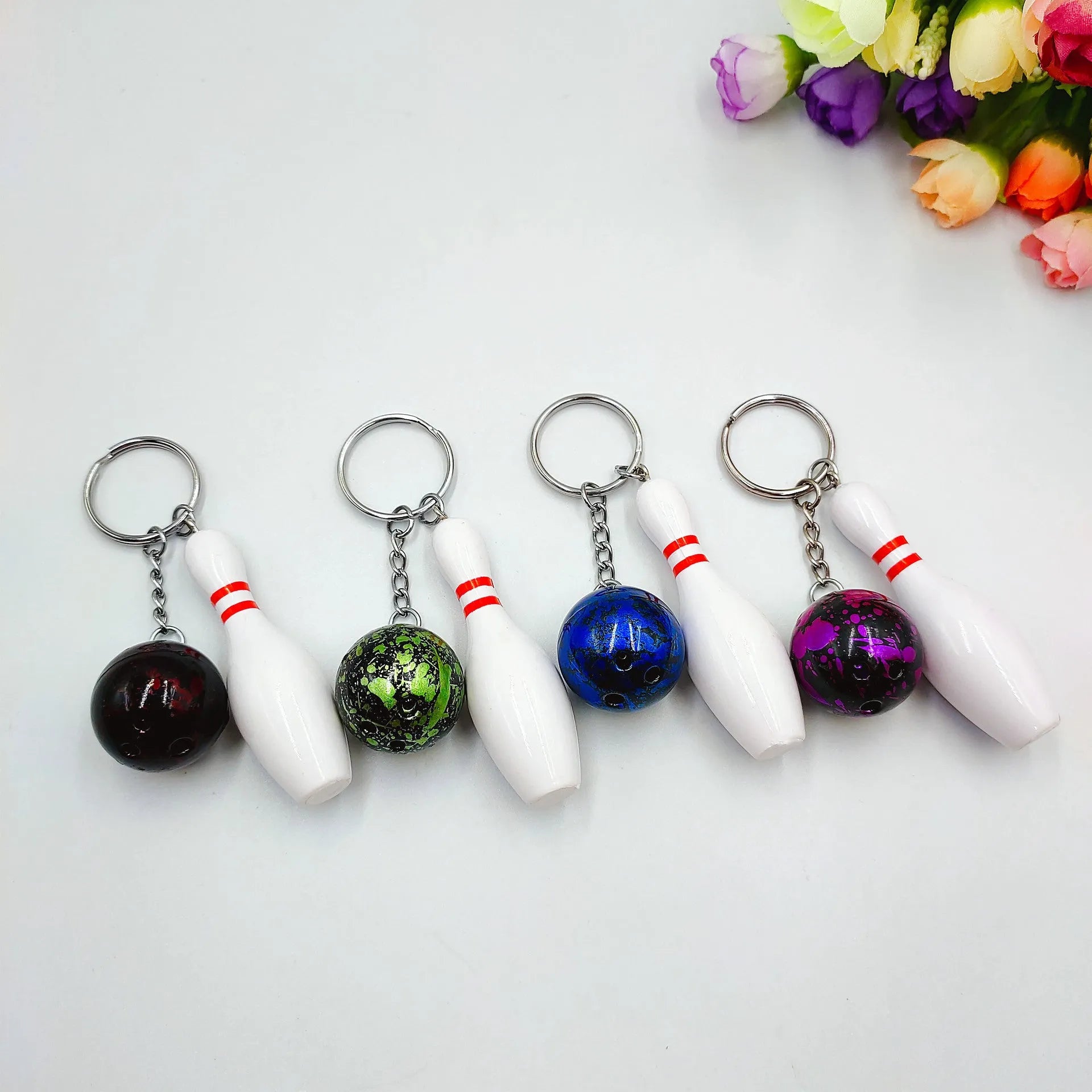 Mini bowling pin keychain pendant in four colours: dark red, blue, purple, green, showing PVC metal construction