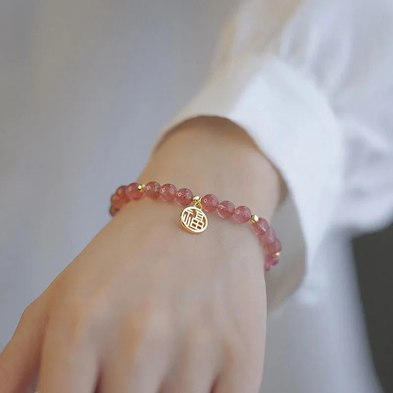 Handmade strawberry quartz style glass bead bracelet with a blessing card charm on a wrist.