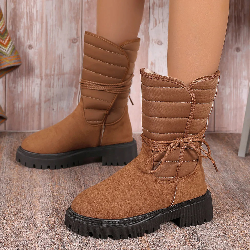 Women's black chunky heel snow boots with suede upper, rubber sole, and lace-up design on wooden floor