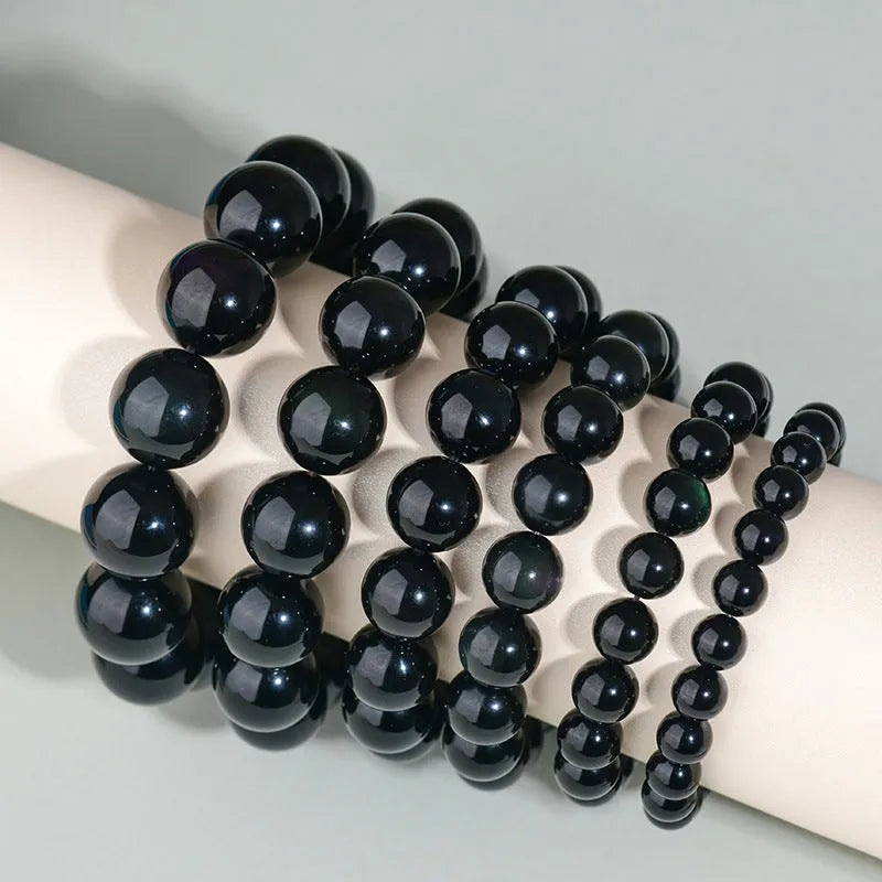 Hand-woven obsidian bracelet with round beads in adjustable sizes from 8mm to 16mm diameter, showing six colour options including black stone and rainbow eye obsidian.