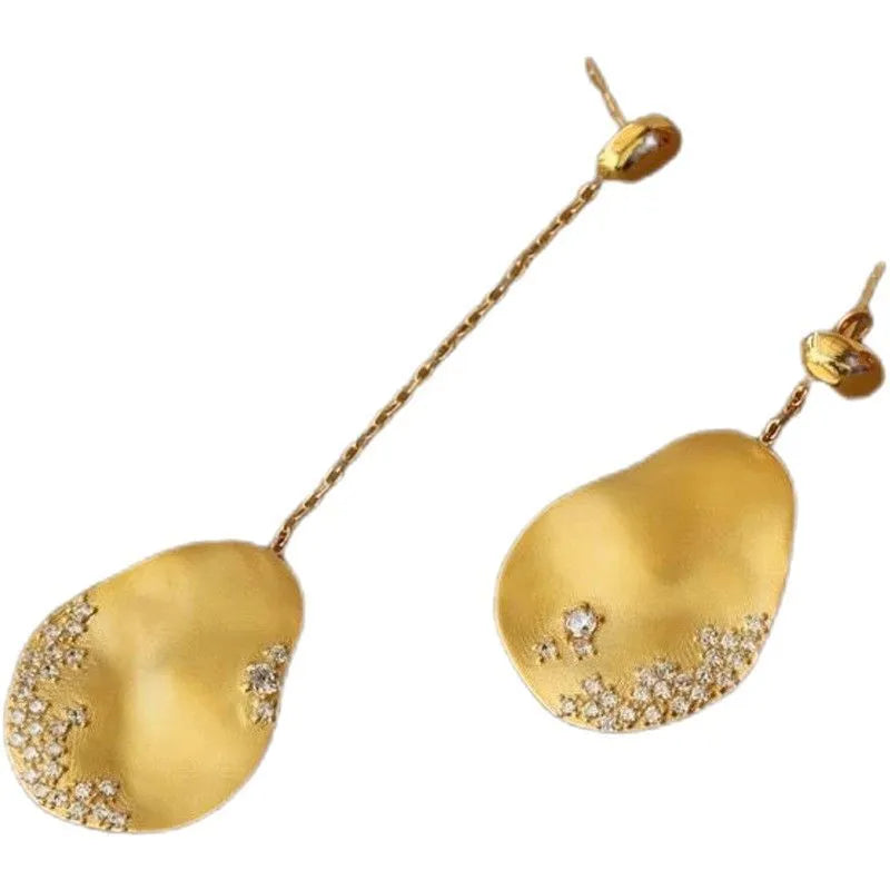 Asymmetric gold and silver floral drop earrings with clear zircon stone detailing on a white background.