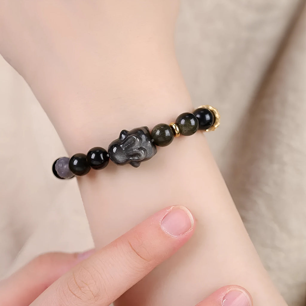 Handmade grey obsidian lying rabbit bracelet with brass and silver details on a wrist, shown in 8mm and 10mm size options.