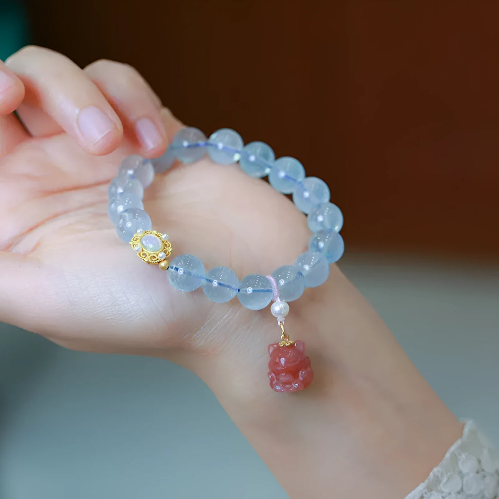 DIY aquamarine Fengjiu charm bracelet components laid out for assembly, showing pearls and pink crystals.