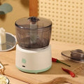 Mini meat grinder with white or light green housing, stainless steel blades, and transparent 225ml cup on anti-slip pad