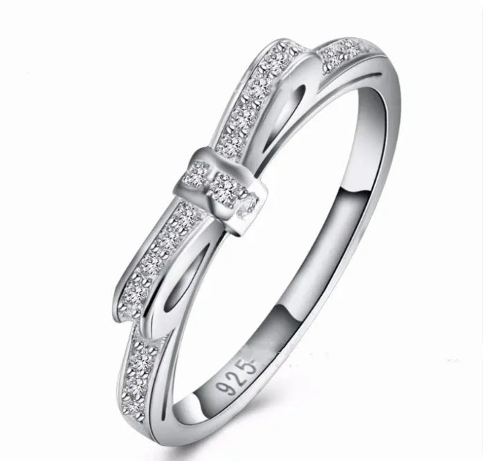 Silver bow-shaped ring with zircon crystal accents on finger, showing electroplated finish and detailed bow structure