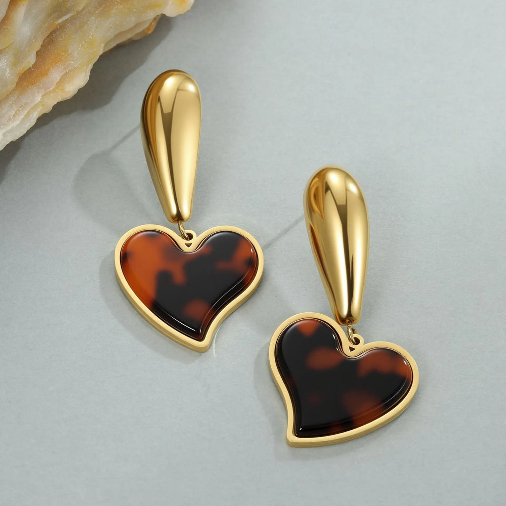 A pair of women's tortoiseshell resin earrings in hawksbill colour, showing heart-shaped and geometric flower designs on stainless steel with 18K plating.