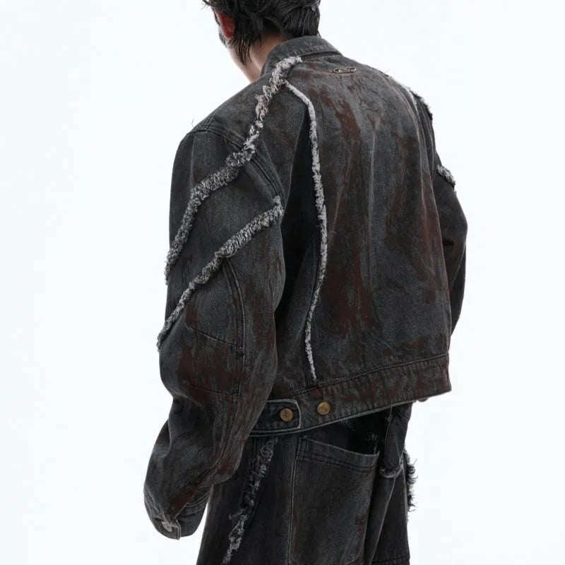 Black gradient denim coat with distressed raw edges and padded shoulders, worn with matching black denim trousers.