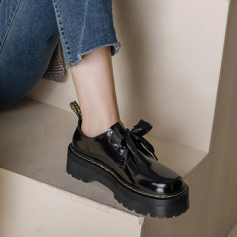 Women's black leather shoes with cross-strap design and thick TPR soles, showing ribbon detailing and lacing closure