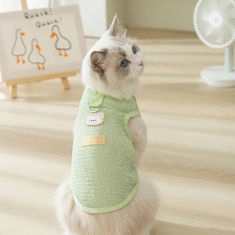 Cat wearing green knitted clothes with a bear patch, showing breathable hollowed-out fabric design.