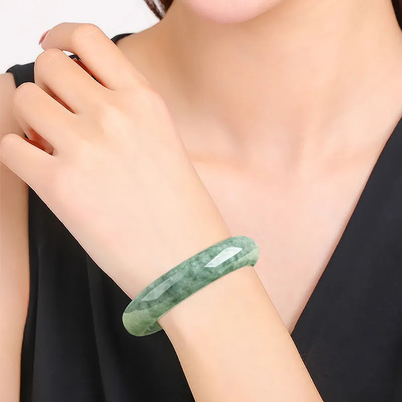 Women's simple bracelet with a natural green emerald bean gemstone on a wrist.