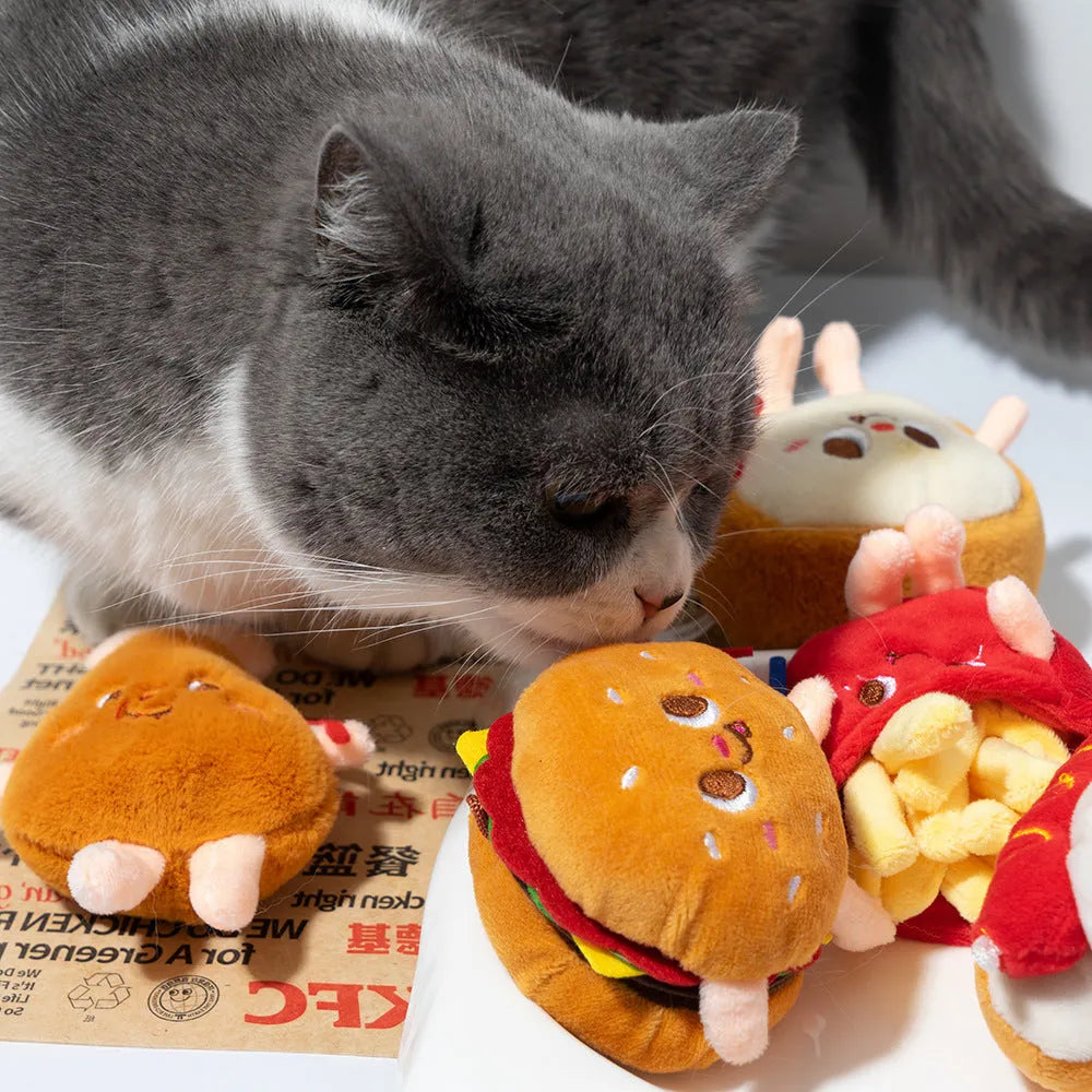 Set of five colourful cat chewing toys shaped like hamburger, chicken legs, fries, hot dog, and bread slice on a white background.