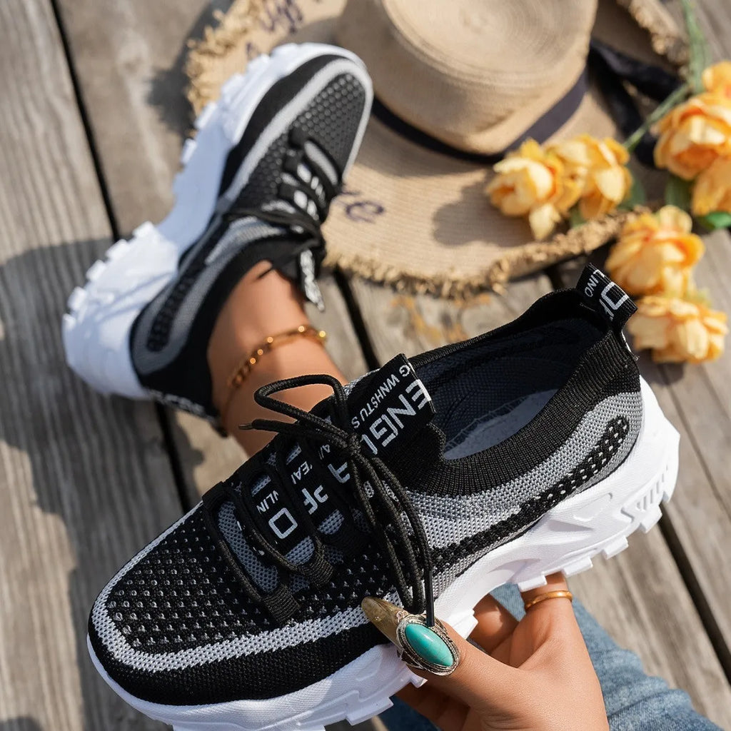 Women's Flyknit mesh sneakers in grey and white, showcasing the breathable upper and flat rubber sole.