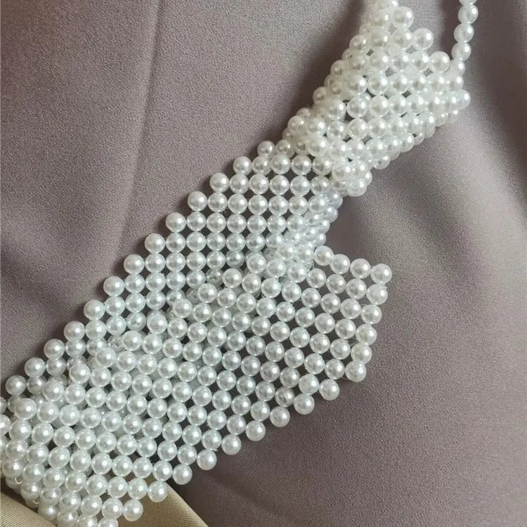 Close-up of a white imitation pearl body chain with an adjustable alloy tie clasp on a dark background.