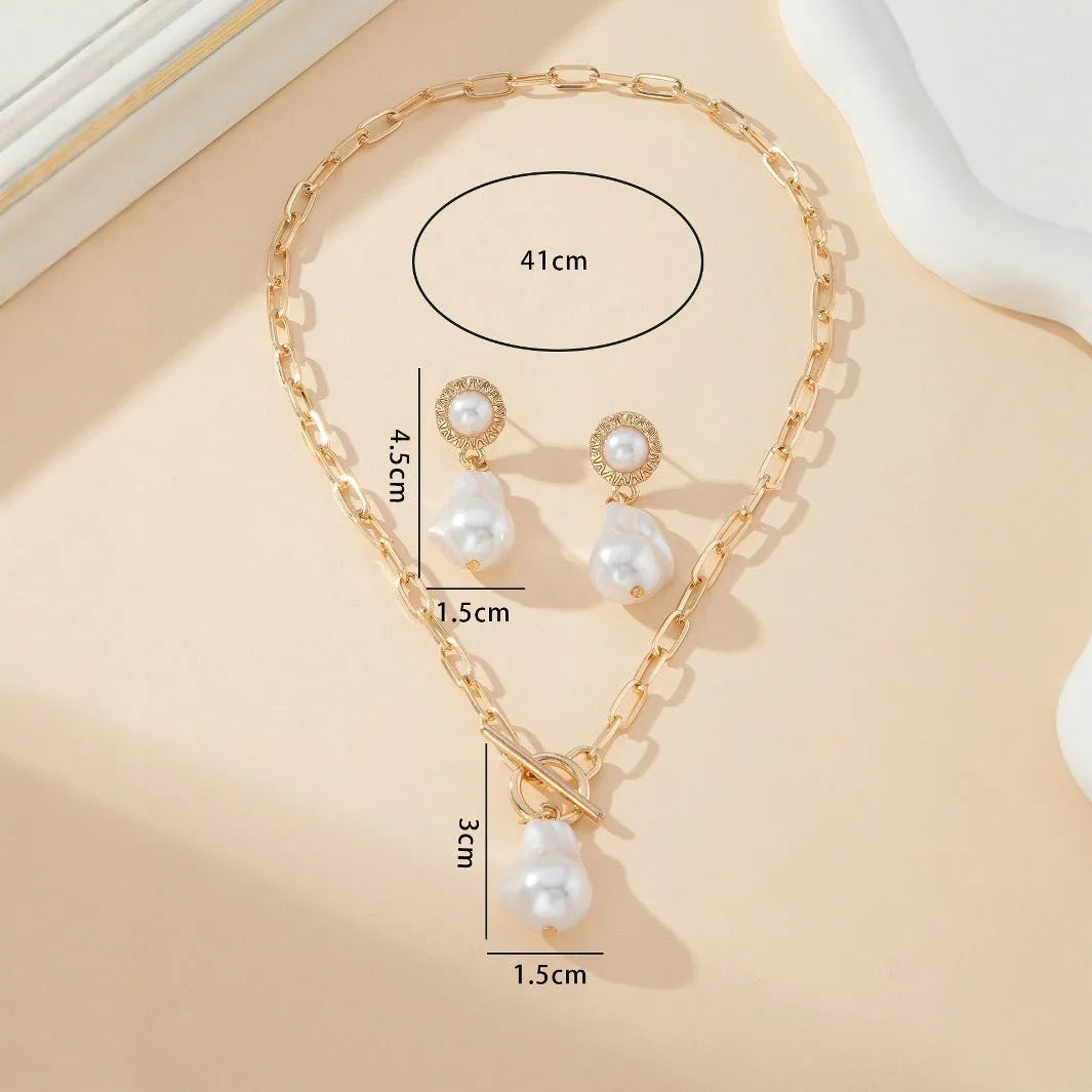 Gold-coloured iron necklace and earrings set with baroque pearl decorative elements on dark background