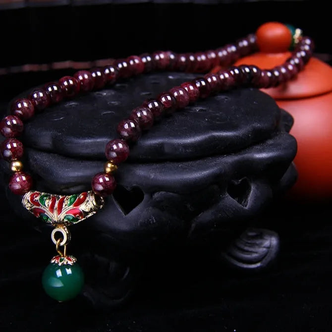 Close-up of a women's bracelet with a 7mm round garnet in a double ring setting and a golden toad charm.