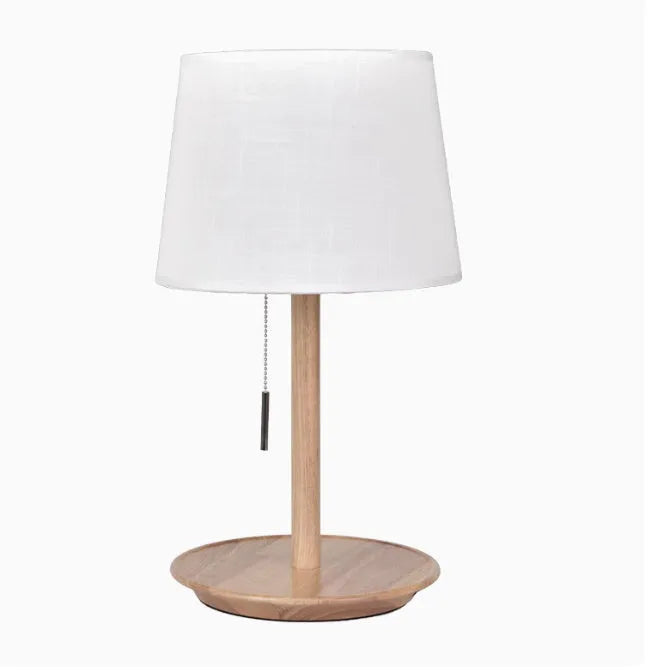 Walnut colour solid wood bedside lamp with a white fabric shade on a wooden surface.