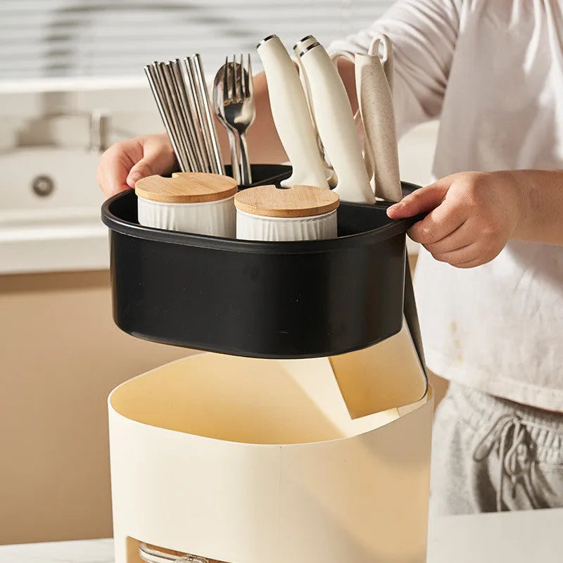 White rotating kitchen storage bucket with utensils next to a four-compartment spice box on a countertop.