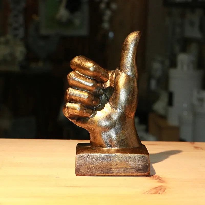 Bronze and silver resin hand gesture ornaments on a wooden desk, showing like, ok, and scissors hand signs.