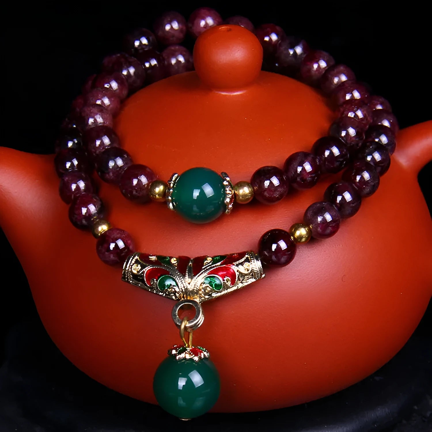 Close-up of a women's bracelet with a 7mm round garnet in a double ring setting and a golden toad charm.