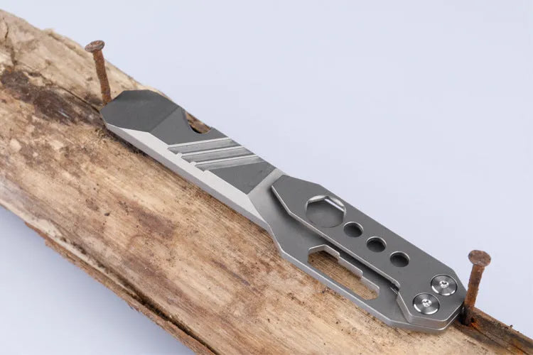 Titanium multi-function crowbar tool with screwdriver tip and bottle opener, shown in stone wash and gun grey finishes.