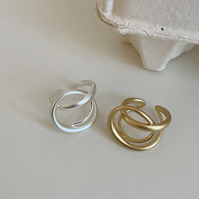 Adjustable geometric open ring with three-dimensional interlaced design and matte finish, shown in gold and silver colour options