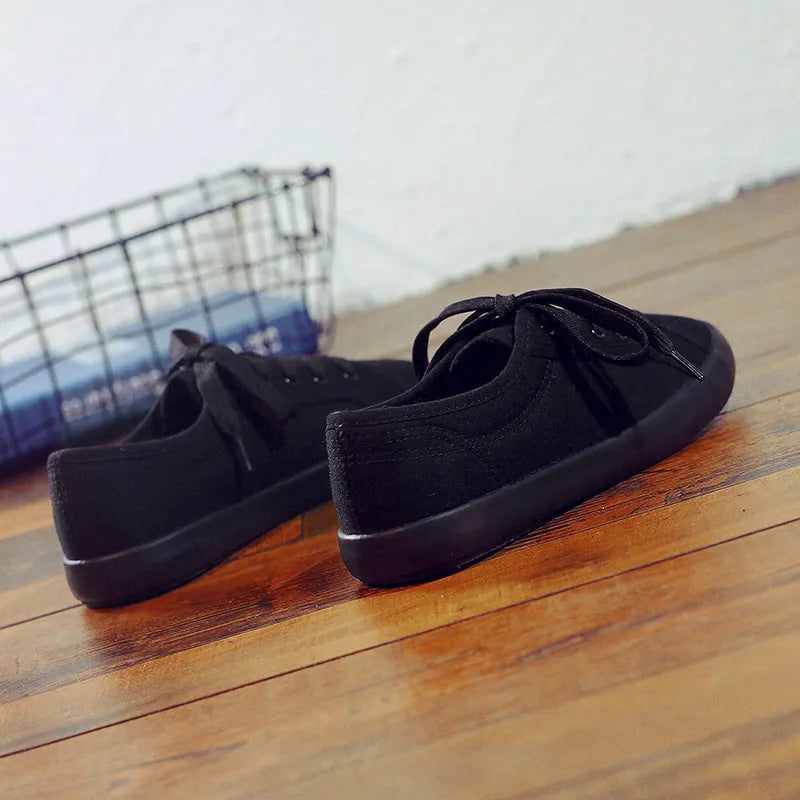 All black low-top canvas lace-up flat shoes for women with a rubber sole.