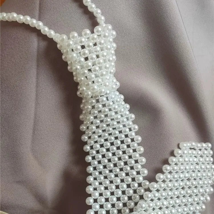 Close-up of a white imitation pearl body chain with an adjustable alloy tie clasp on a dark background.