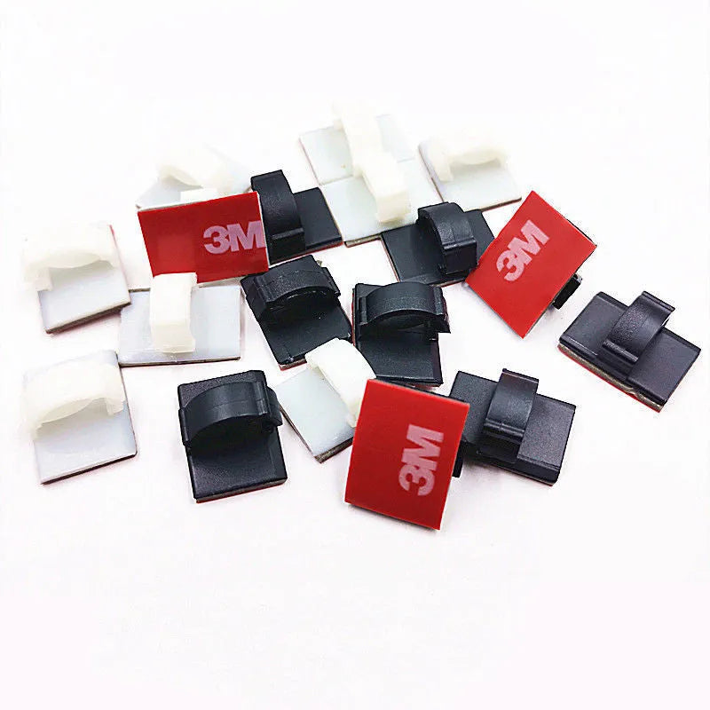 Black and white plastic self-adhesive cable clamps for wire management on a table.