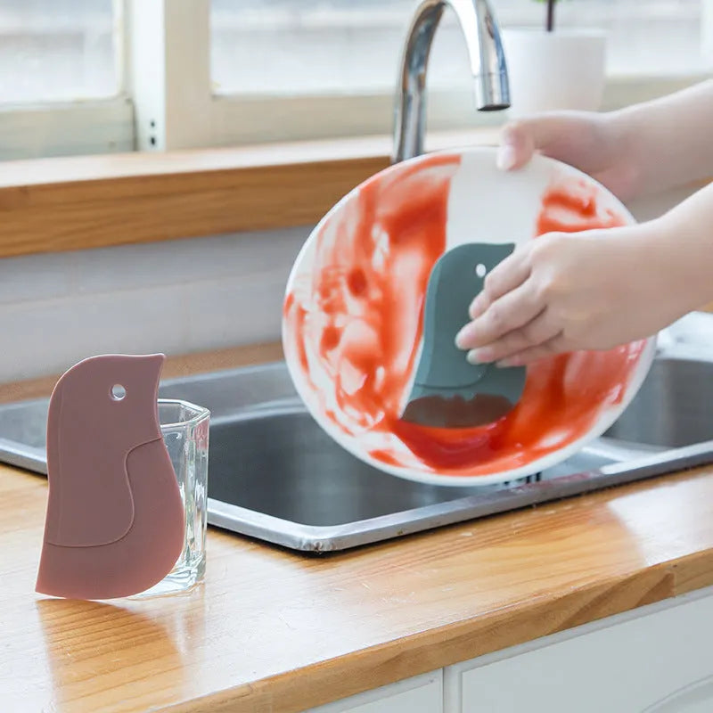 Green penguin-shaped kitchen scraper with soft blade, 11cm by 7cm, for cleaning plates and pots