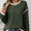 Beige loose drop shoulder knit top with green four-leaf clover design and contrast trim on neckline.