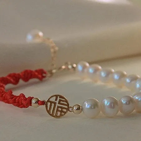 Women's pearl bracelet with braided red rope and gold plated fu character charm